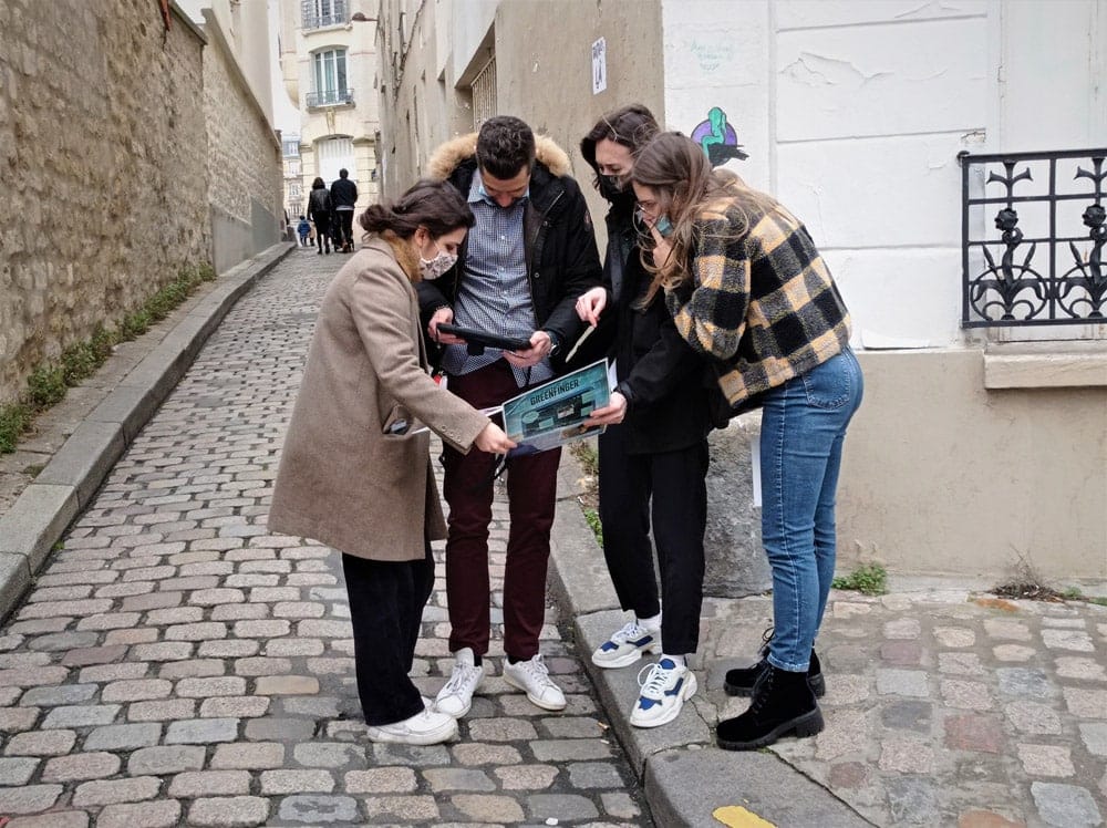 4 adultes dans les rues de Rueil se regroupent autour d'une tablette numérique pour résoudre une énigme