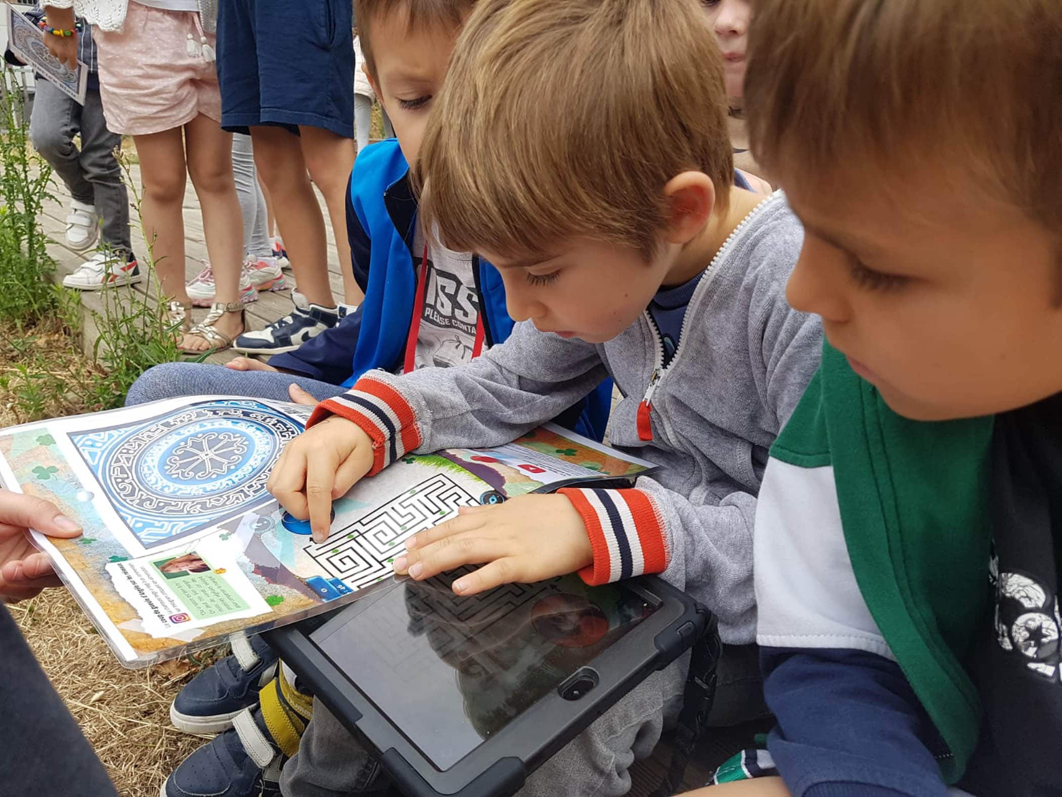 Des enfants de 7 ans appartenant à un centre aéré essayent de résoudre une énigme sur une tablette pendant un jeu de piste