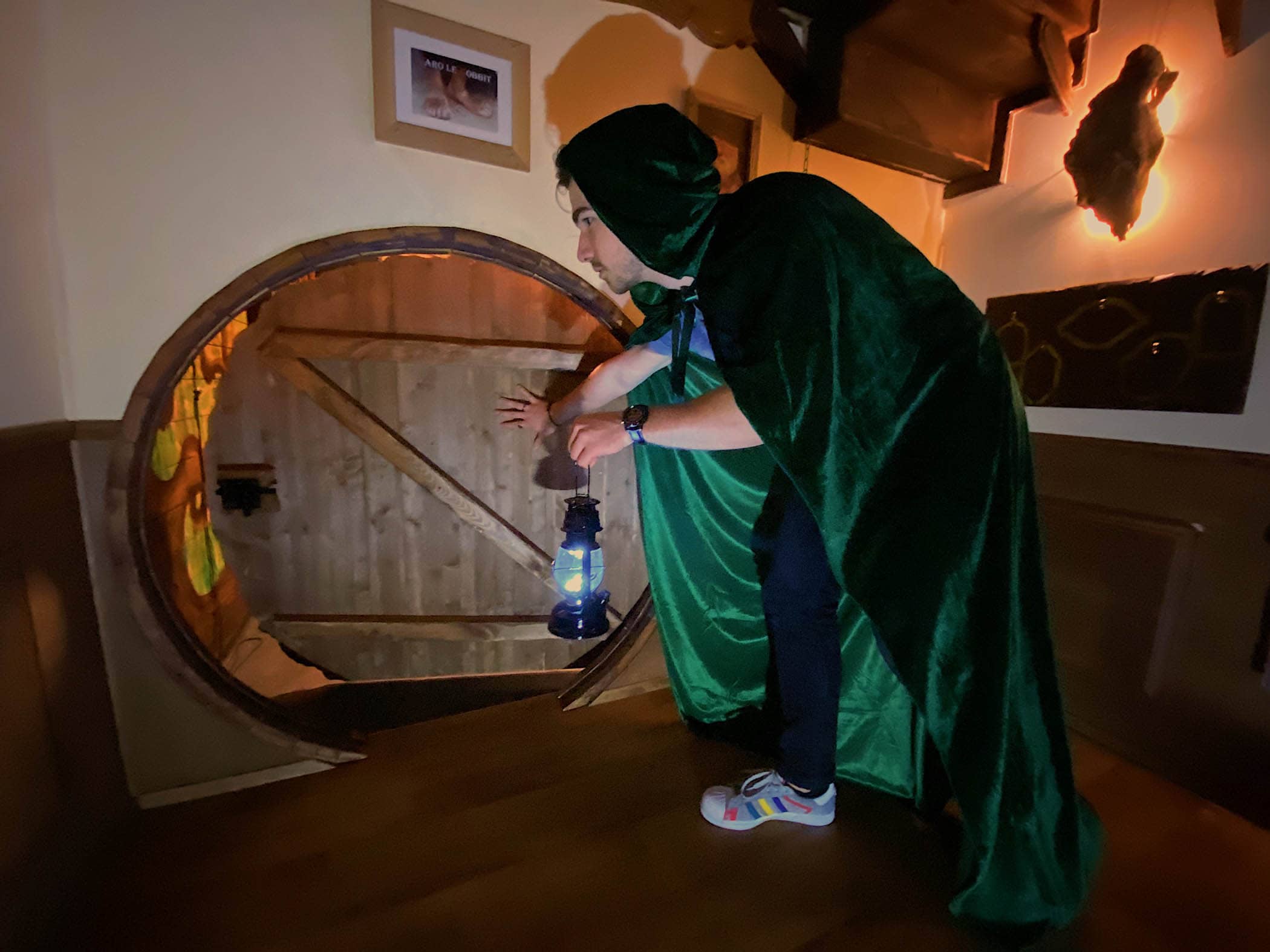 Un joueur portant une cape ouvre une "porte de Hobbit" lors d'un Escape Game inspiré du Seigneur des Anneaux