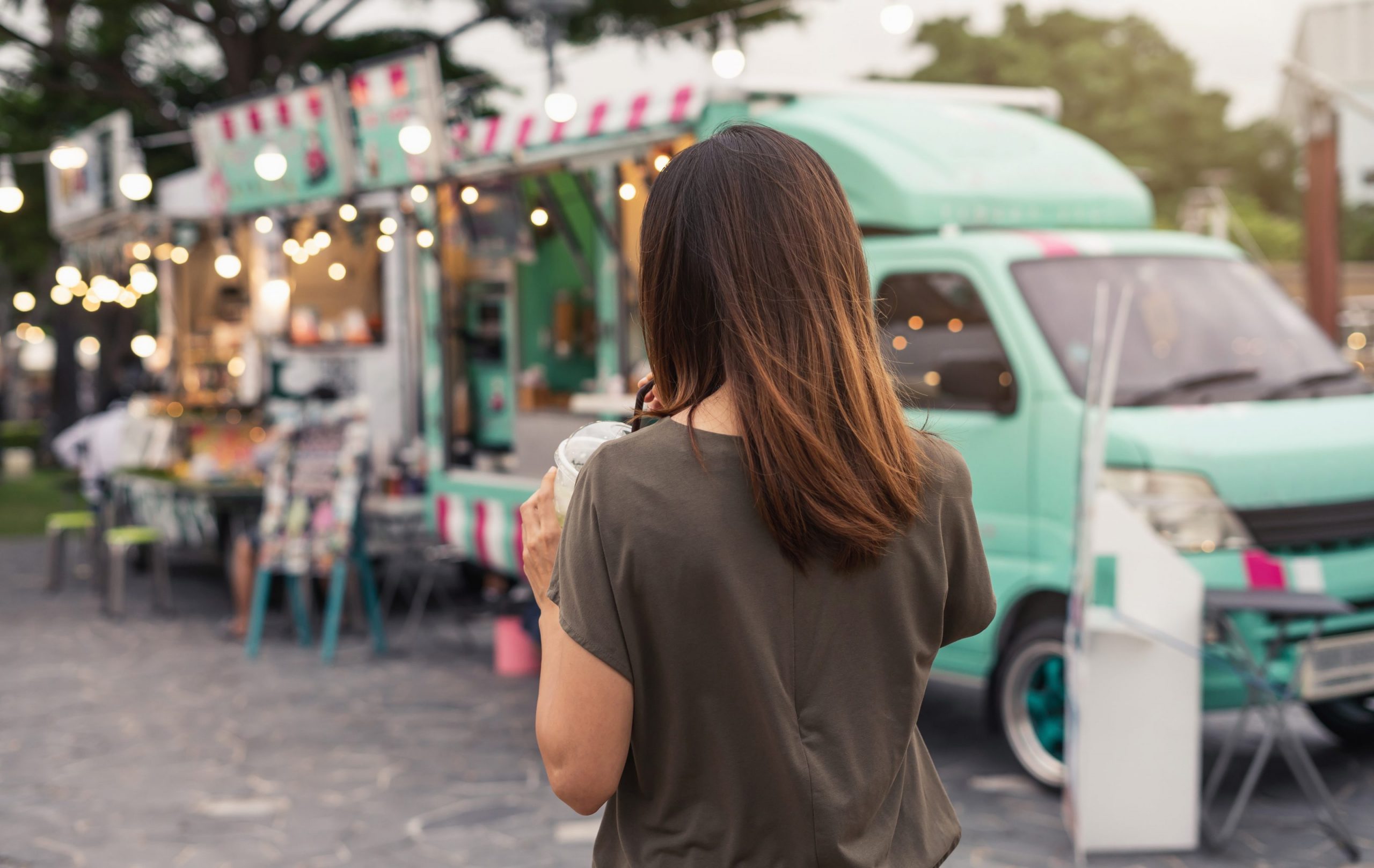 Une jeune femme de dos buvant un milk-shake devant un food truck